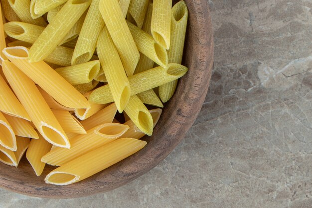 Yellow and green penne pasta in wooden bowl.