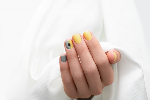 Yellow and grey nail design. Manicured female hand on white fabric background.