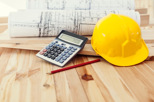 Yellow helmet with blueprints and calculator on wood