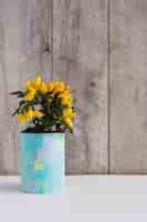 Free photo yellow hot chili peppers in painted container on the table against wooden wall