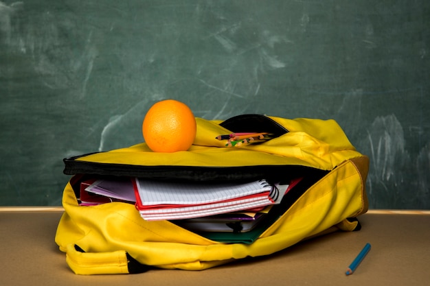 Free photo yellow knapsack with copybooks and orange