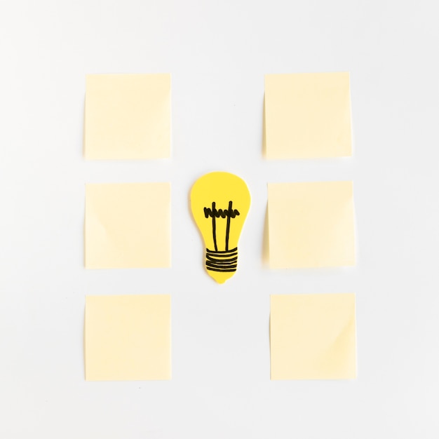 Free photo yellow light bulb between adhesive notes arranged in a row