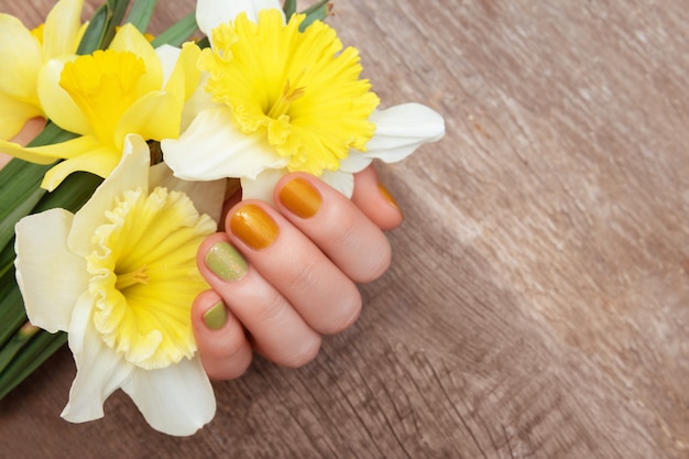 Yellow nail design. Female hand with glitter manicure holding narcissus flowers.