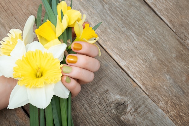 Yellow nail design. Female hand with glitter manicure holding narcissus flowers.