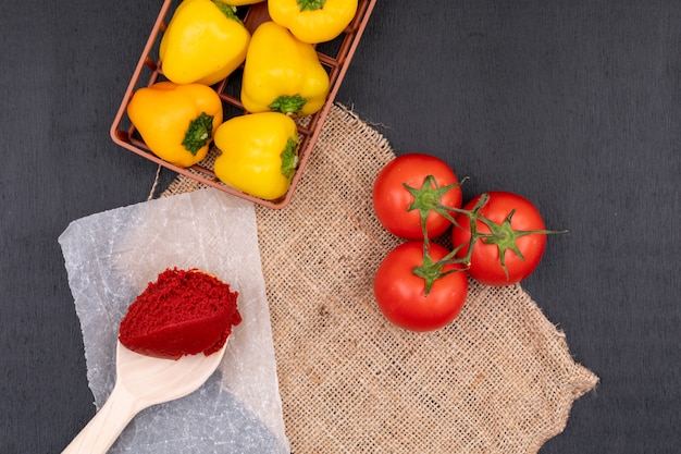 yellow pepper in basket near a bunch of tomatoes and tomato paste in spoon on black