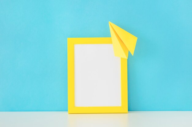 Yellow photo frame and paper plane in front of blue wall