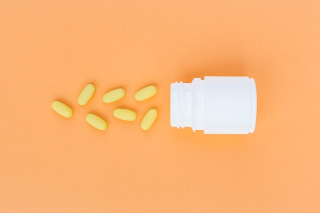 Yellow pills spilled from white plastic bottle on an orange background