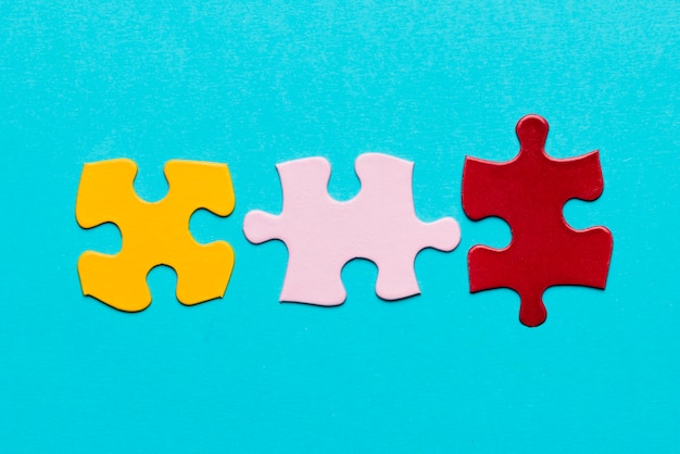 Free Photo yellow; pink and red jigsaw puzzle piece on blue textured background