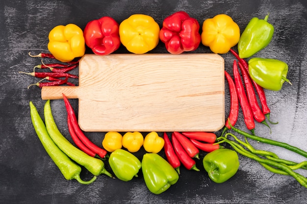 Yellow, red, green sweet pepper and chili peppers around the cutting board