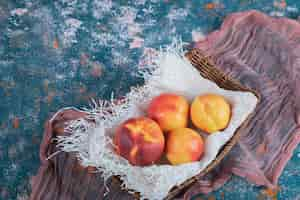 Free photo yellow red peaches on wooden basket on piece of white burlap.