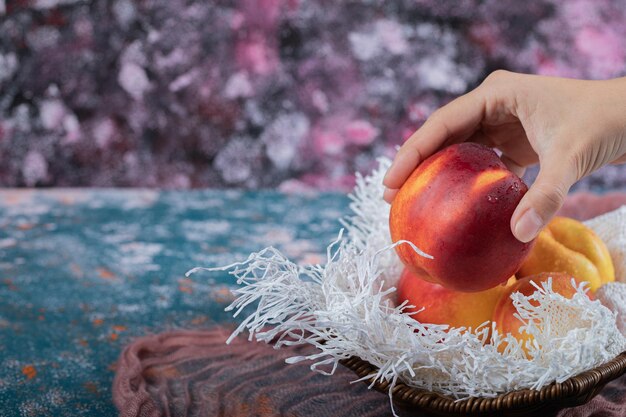 Yellow red peaches on wooden basket on piece of white burlap.