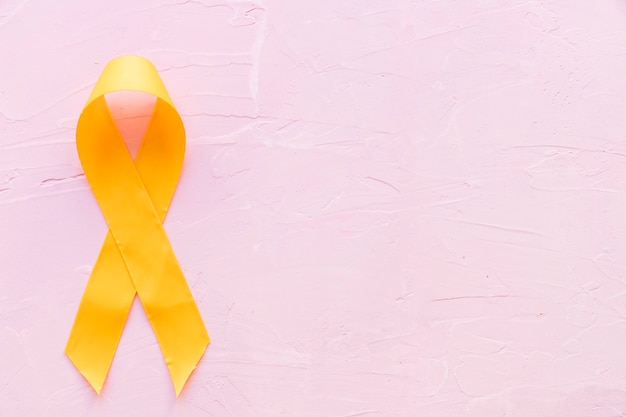 Free photo yellow ribbon symbolic color for sarcoma bone cancer on pink backdrop