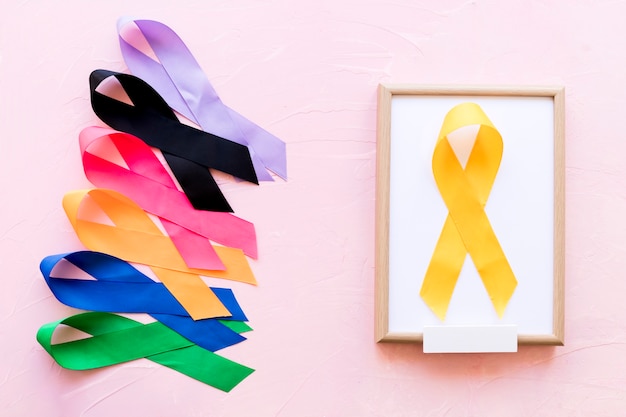 Yellow ribbon on white wooden frame near the row of colorful awareness ribbon