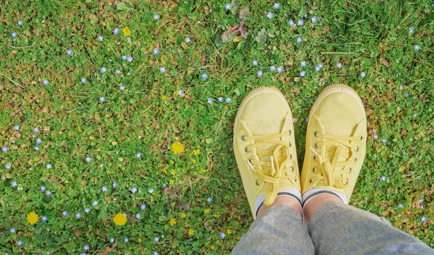 Yellow sneakers on a green spring meadow with yellow flowers the beginning of spring and travel time first person point of view top view with copy space idea for background or postcard