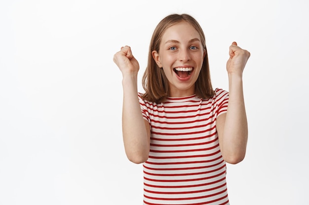 Free Photo yes hooray. happy blond girl cheering, raising hands up and scream yes, smiling broadly, celebrating victory, achieve goal or win prize, triumphing, white background