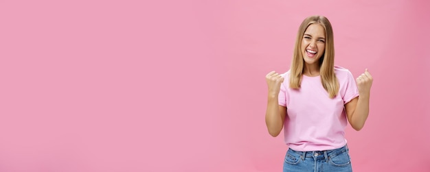 Free Photo yes i did it portrait of happy delighted successful young female student receiving award triumphing being excited and joyful raising clenched fists in cheer gazing confident at camera over pink wall