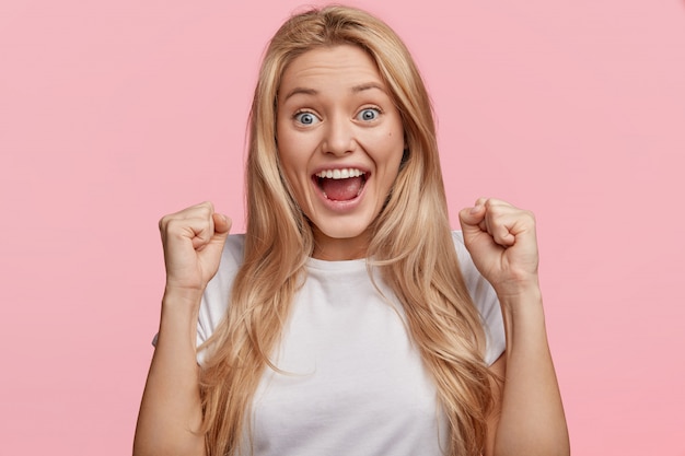 Free Photo yes, i done it! excited cheerful female model with joyful expression, cheers and clenches fists, celebrates her success, has appealing look, poses against pink wall achievement