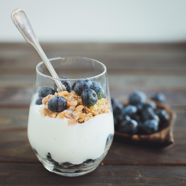 Free photo yogurt with granola and fresh blueberries in glass bowl over old wood background vintage effect