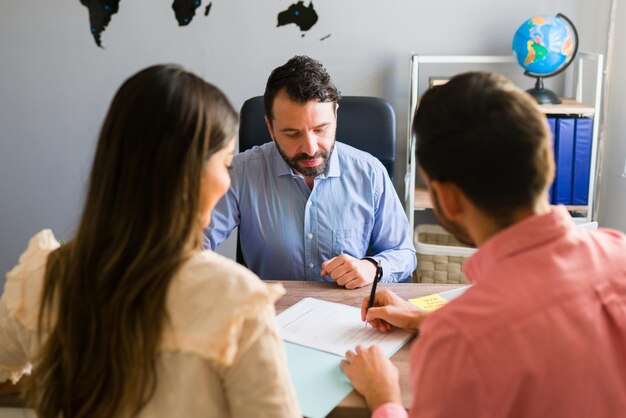 You got a deal. Young man signing a sales contract for a holiday vacation with his wife. Sales representative closing a deal for a timeshare sale with some customers at the travel agency