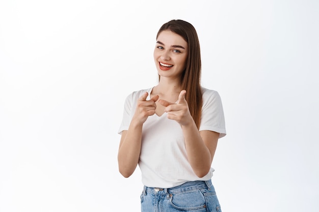 You got this, join us. Smiling assertive woman pointing at front, inviting to work for company, or to event, praising good job, well done gesture, standing over white wall