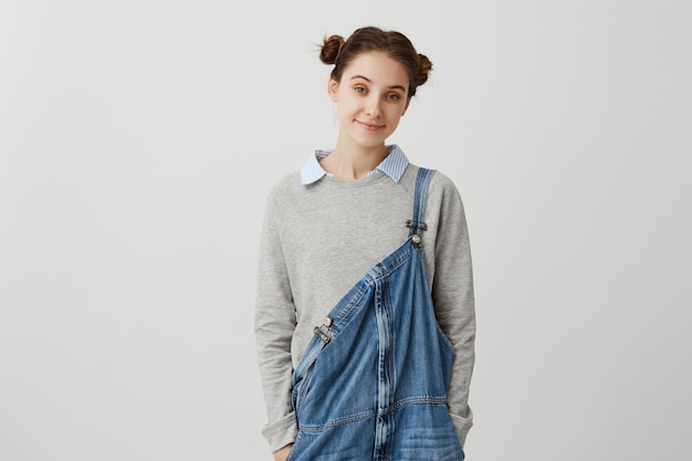 Free photo young adorable woman looking  in casual denim jumpsuit. affable brunette lady with hair in double buns enjoying time staying at home on weekend. coziness concept