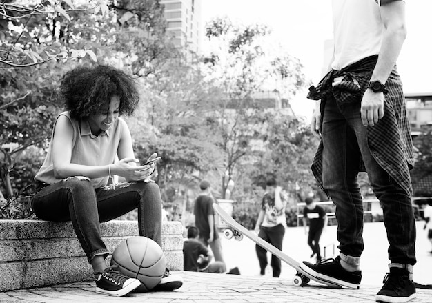 Young adult friends chilling at the park using smartphones and skateboarding 