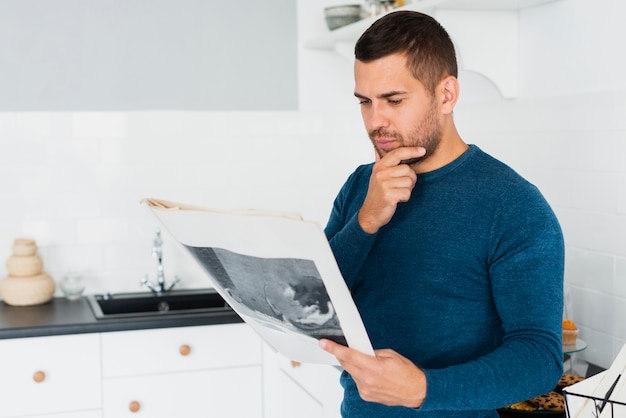 Young adult is reading the newspaper in the kitchen