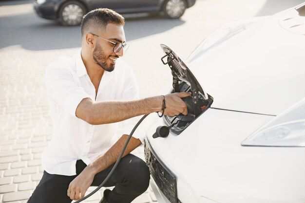 Young adult man charging his electric car in the city. Eco electric car concept.