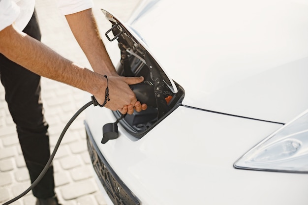 Free photo young adult man charging his electric car in the city. eco electric car concept.