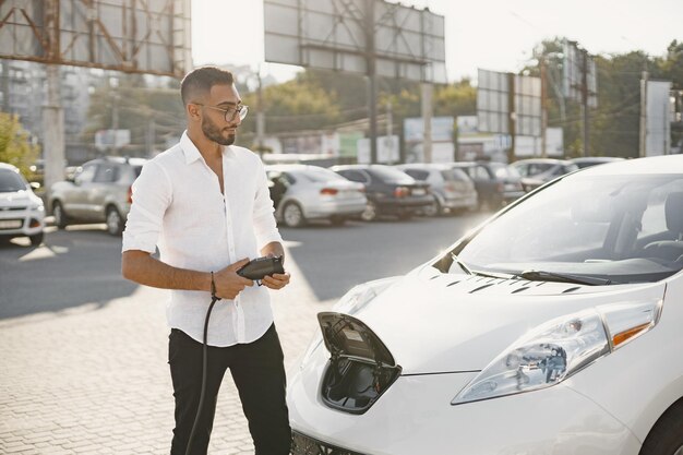 Young adult man charging his electric car in the city. Eco electric car concept.