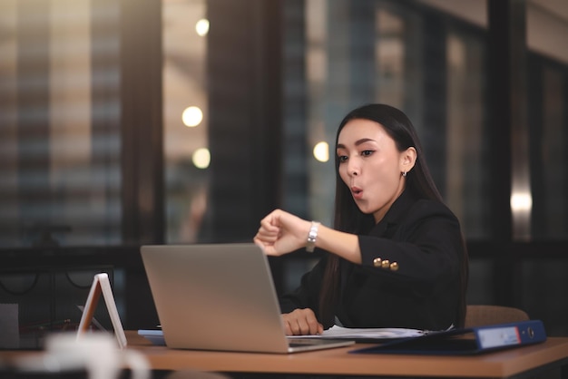 Young adult smart asian business woman in black casual suit using laptop working overtime in urban office