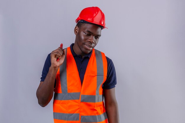 Young african american builder man wearing construction vest and safety helmet holding adjustable wrench looking aside with smile on face standing 