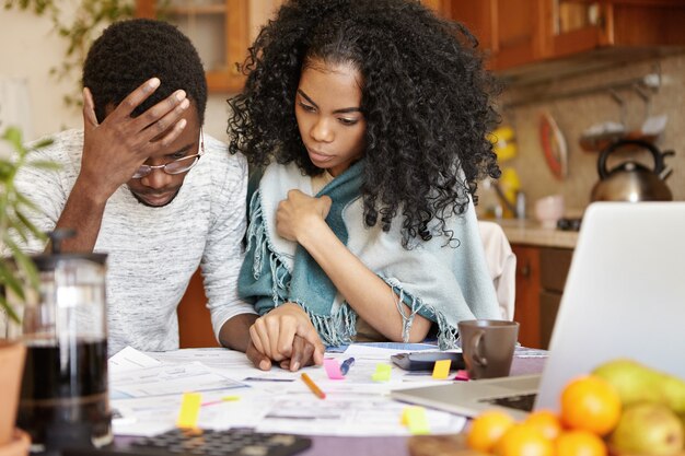 Young African-American couple with many debts calculating gas and electricity bills