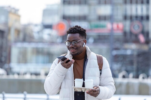 Young African American entrepreneur business man holding coffee in cardboard cup and talking on phone