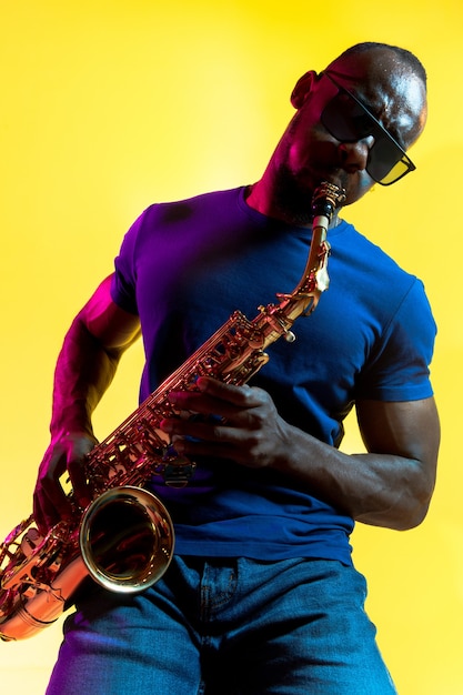 Free Photo young african-american jazz musician playing the saxophone on yellow background in trendy neon light.