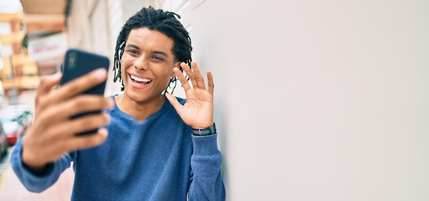 Young african american man doing video call using smartphone leaning on the wall