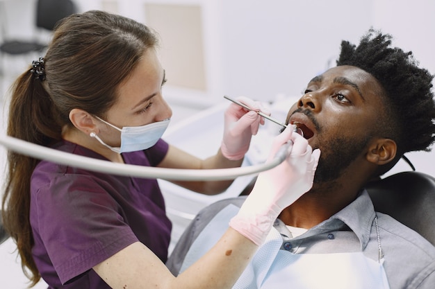 Young african-american man. Guy visiting dentist's office for prevention of the oral cavity. Man and famale doctor while checkup teeth.