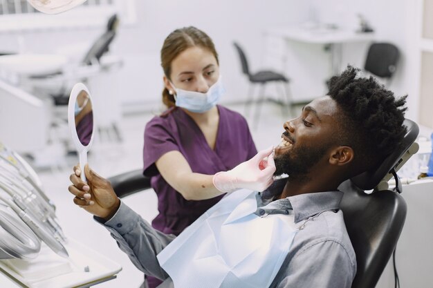 Young african-american man. Guy visiting dentist's office for prevention of the oral cavity. Man and famale doctor while checkup teeth.