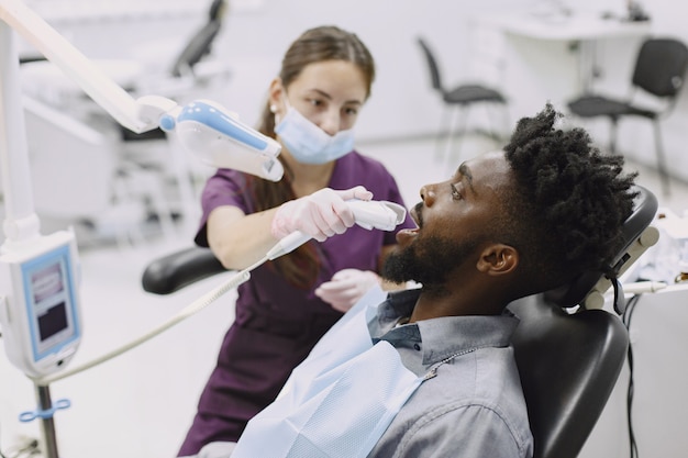 Young african-american man. Guy visiting dentist's office for prevention of the oral cavity. Man and famale doctor while checkup teeth.