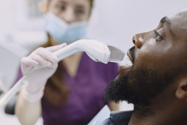 Young african-american man. Guy visiting dentist's office for prevention of the oral cavity. Man and famale doctor while checkup teeth.