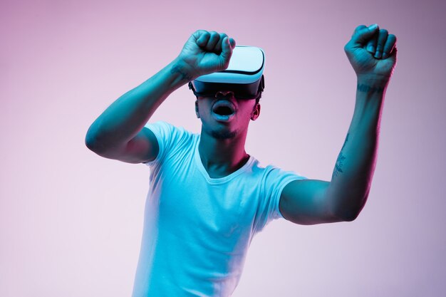 Young african-american man's playing and using VR-glasses in neon light on gradient background