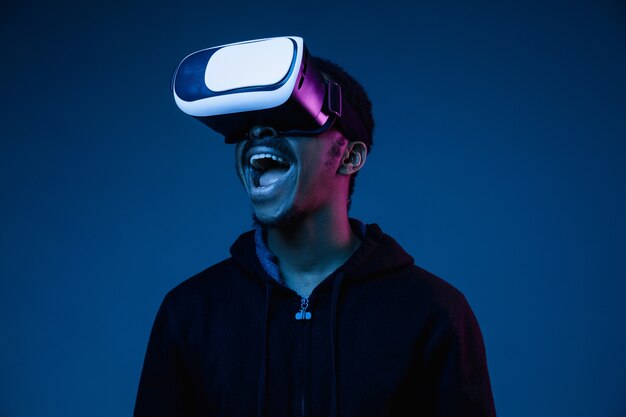 Young african-american man's playing in VR-glasses in neon light on gradient