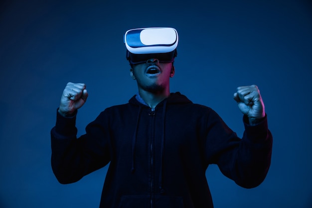 Young african-american man's playing in VR-glasses in neon light on gradient