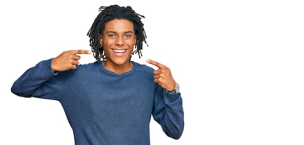 Young african american man wearing casual winter sweater smiling cheerful showing and pointing with fingers teeth and mouth dental health concept