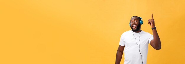 Young african american man wearing headphone and enjoy music dancing over yellow gold background