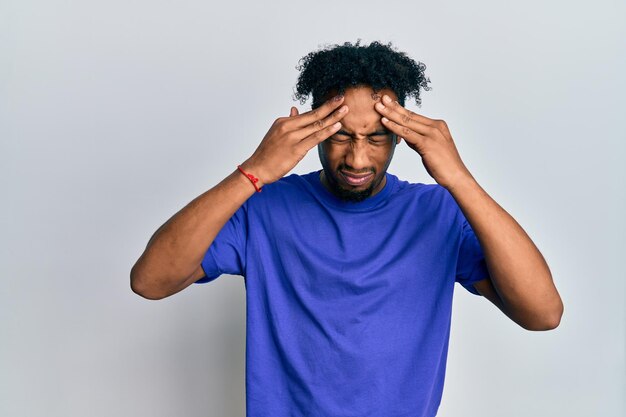 Young african american man with beard wearing casual blue t shirt with hand on head, headache because stress. suffering migraine.