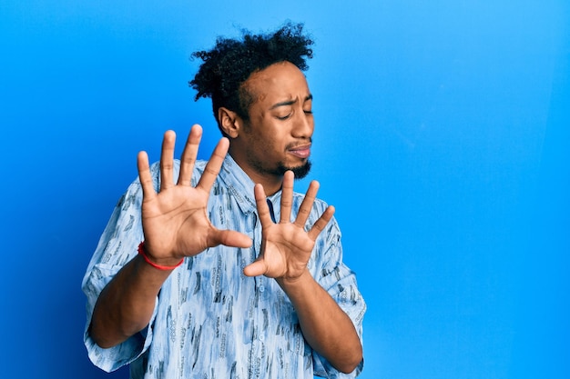 Young african american man with beard wearing casual clothes disgusted expression displeased and fearful doing disgust face because aversion reaction with hands raised