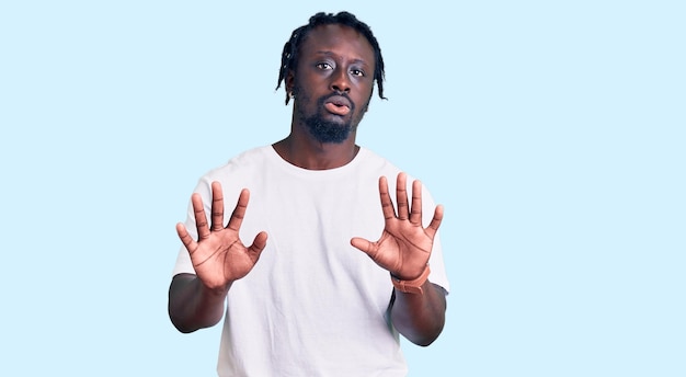 Young african american man with braids wearing casual white tshirt moving away hands palms showing refusal and denial with afraid and disgusting expression stop and forbidden