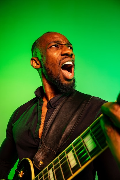 Free Photo young african-american musician playing the guitar like a rockstar on gradient green-yellow background.