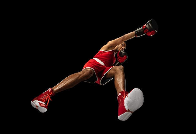 Young african-american professional boxer in action, motion isolated on black wall, look from the bottom. Concept of sport, movement, energy and dynamic, healthy lifestyle. Training, practicing.